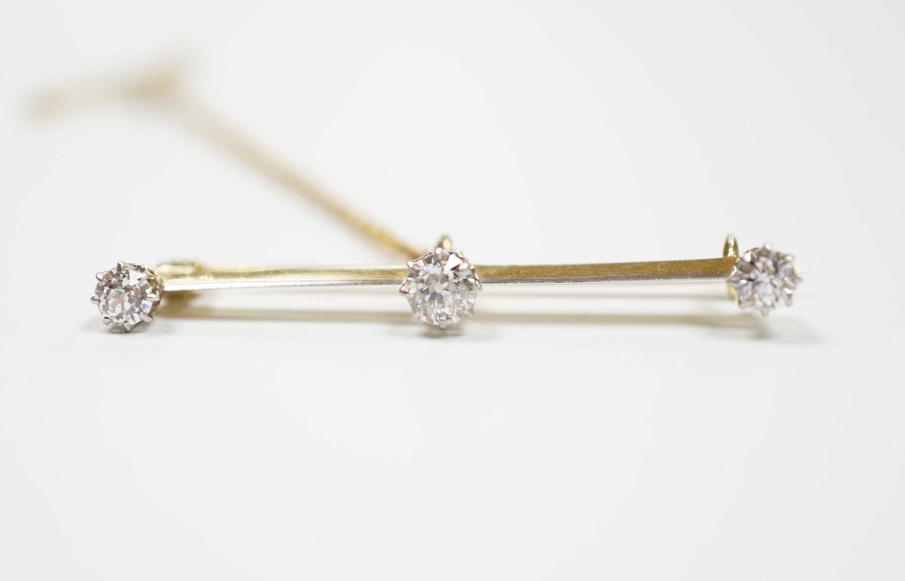 A yellow metal and three stone diamond set bar brooch, 37mm, with safety chain, gross weight 3 grams.